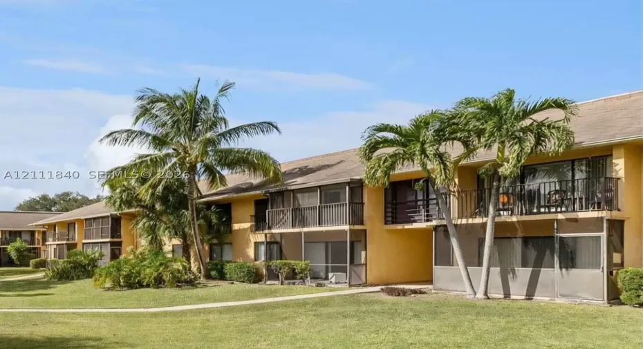 Stucco exterior featuring screened-in lanais, private balconies with metal railings, and mature palm trees situated on landscaped grounds