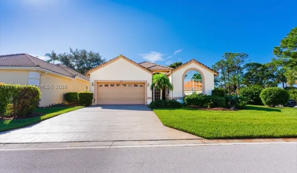 Stucco exterior featuring a tiled roof, arched window, multi-car garage, and paved driveway