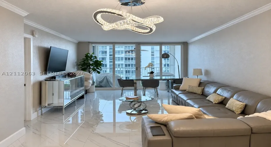Polished tile flooring with subtle veining, contemporary geometric crystal chandelier, and floor-to-ceiling glass sliding doors opening to a private balcony