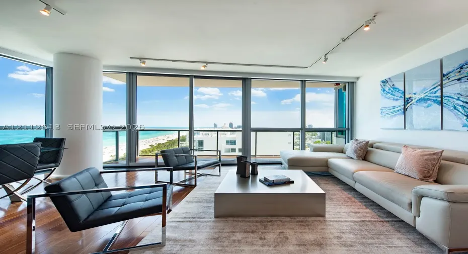 Floor-to-ceiling glass windows, wood-finish flooring, recessed track lighting, and a private balcony
