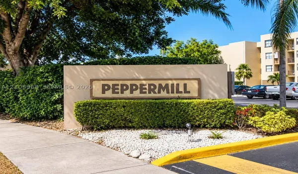 Peppermill community entrance featuring a stucco monument sign, mature landscaping, decorative stone ground cover, and concrete curbing