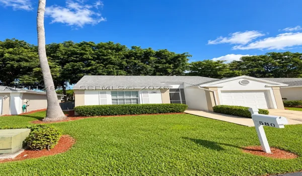 Stucco exterior featuring an attached single-car garage, manicured landscaping, and a covered entryway