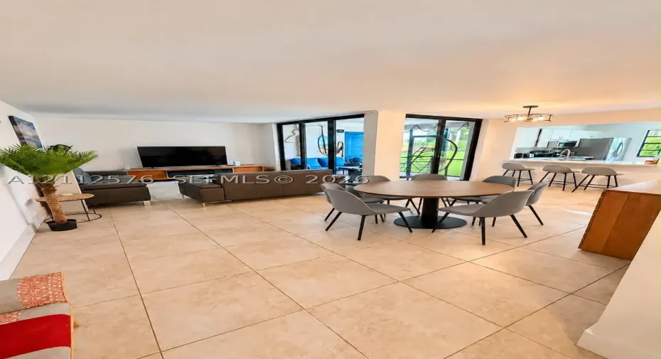 Open-concept living space featuring large-format tile flooring, expansive floor-to-ceiling glass sliding doors, and a kitchen pass-through with an integrated breakfast bar