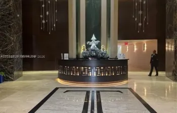 Grand lobby featuring stone flooring with inlaid detailing, dark stone accent walls, a curved reception desk with integrated lighting, and tiered crystal light fixtures