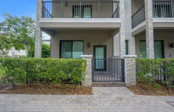 Multi-story exterior featuring stone veneer accents, a gated private entrance, paver walkway, and an upper-level balcony with metal railing