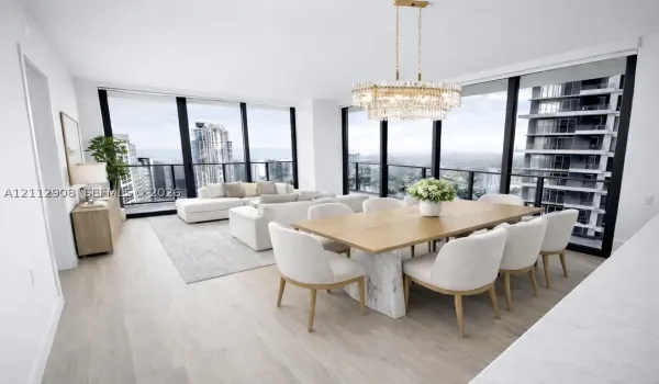 Open-concept floor plan featuring floor-to-ceiling windows, wood-finish flooring, and a multi-tiered crystal chandelier