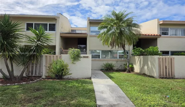 Stucco exterior townhome featuring multi-level architecture, concrete walkways, private vertical wood fencing, and mature landscaping