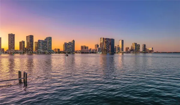 Waterfront property featuring a private dock and direct water access, showcasing a expansive cityscape backdrop at dusk