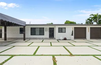 Single-story exterior featuring white stucco finish, dual brown garage doors, a covered carport, and concrete paver driveway with integrated turf strips