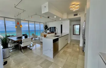 Open-concept kitchen featuring an island with a stone-finish countertop, stainless steel appliances, floor-to-ceiling windows, and natural stone flooring throughout