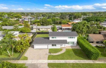 Two-story residence featuring a multi-pitched shingled roof, white exterior siding, paved driveway, paver walkway, and established perimeter landscaping