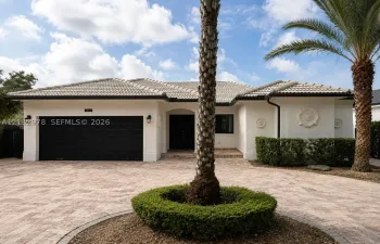 Exterior featuring a white stucco facade, a multi-car garage with black doors, a tile roof, decorative wall medallions, and a paved circular driveway