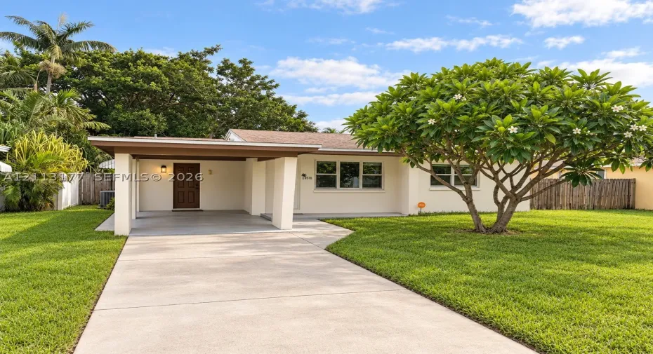Exterior facade featuring a covered carport, concrete driveway, and expansive lawn with mature landscaping