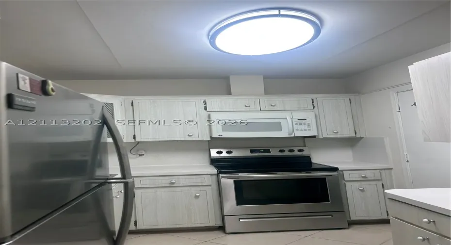 Kitchen featuring light-finish cabinetry, stainless steel refrigerator and range, over-the-range microwave, and overhead flush-mount lighting