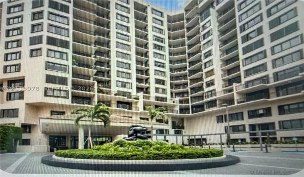Multi-story high-rise exterior featuring private recessed balconies, a circular driveway entrance, a covered porte-cochère, and a central landscaped island with sculptural focal point