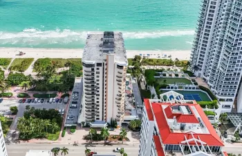 High-rise residential building featuring multiple private balconies, direct coastal frontage, paved surface parking, and shared tennis courts