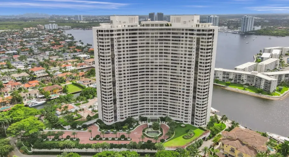High-rise building featuring a curved architectural design, expansive glass balconies, a circular paved motor court with a central fountain, and landscaped green space