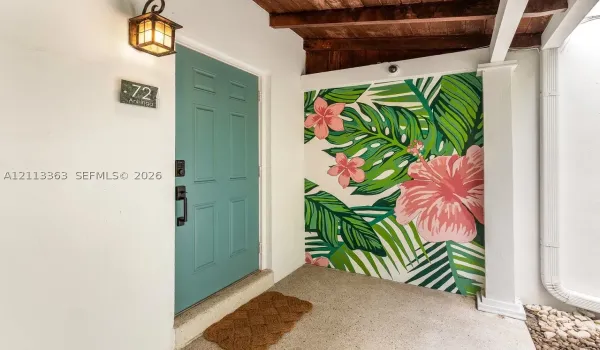 Entryway featuring a solid teal six-panel door, custom floral wall mural, exposed wood ceiling beams, and a wall-mounted lantern-style fixture