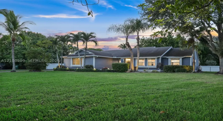 Single-story residence featuring horizontal lap siding, a shingled roof, multi-pane windows, and extensive mature landscaping