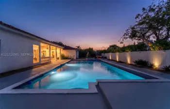 Rectangular in-ground swimming pool featuring a perimeter stone coping, concrete patio, covered patio area, and perimeter privacy fencing