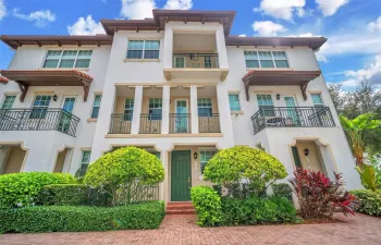 Stucco multi-story exterior featuring a tile roof, multiple wrought-iron balconies, arched entryway detailing, and brick-paver hardscaping