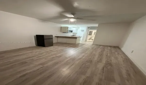 Open-concept room featuring light wood-finish flooring, white cabinetry, a countertop workstation, and a ceiling fan