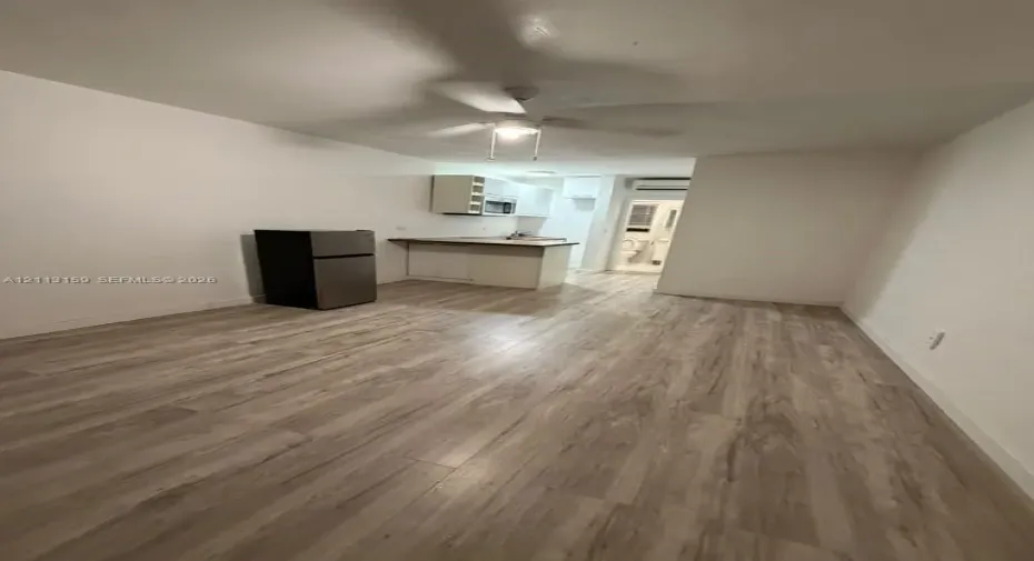 Open-concept room featuring light wood-finish flooring, white cabinetry, a countertop workstation, and a ceiling fan