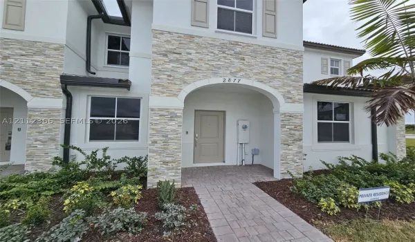 Stucco exterior featuring stacked stone accents, arched entryway, paved walkway, and multi-pane windows