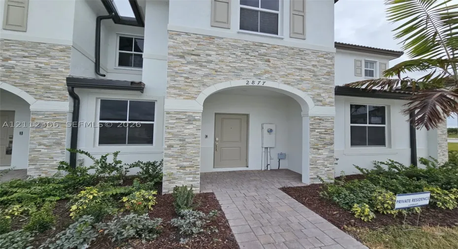 Stucco exterior featuring stacked stone accents, arched entryway, paved walkway, and multi-pane windows