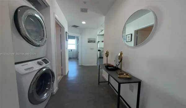 Dedicated laundry area featuring a stacked washer and dryer unit, neutral flooring, recessed lighting, and a circular wall-mounted mirror