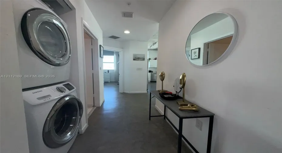 Dedicated laundry area featuring a stacked washer and dryer unit, neutral flooring, recessed lighting, and a circular wall-mounted mirror