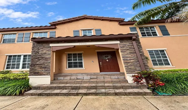Stucco exterior facade featuring stone veneer detailing, a covered entryway with corbel accents, multi-pane windows with shutters, and masonry steps