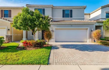 Two-story stucco exterior featuring a paved driveway, tile roof, and decorative shutters