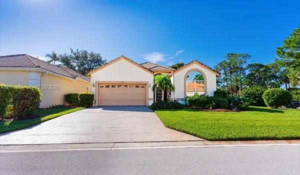 Stucco exterior featuring a tiled roof, arched window, multi-car garage, and paved driveway