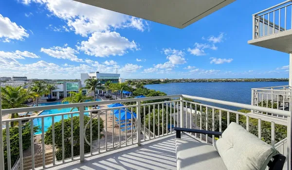 Private balcony featuring metal railings and concrete flooring, overlooking a swimming pool, mature palm trees, and waterfront scenery