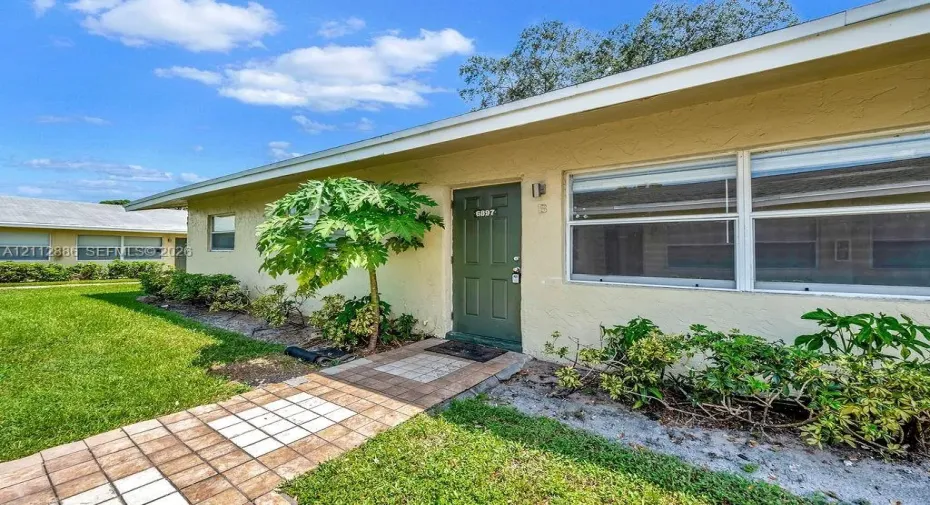 Stucco exterior featuring a paved walkway, paneled front door, and manicured landscaping