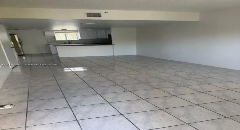 Open-concept interior featuring light-colored ceramic tile flooring, white cabinetry, a peninsula counter, and stainless steel kitchen appliances