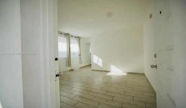 Interior space featuring neutral wall tones, light-colored tile flooring, and a multi-panel door with metallic hardware