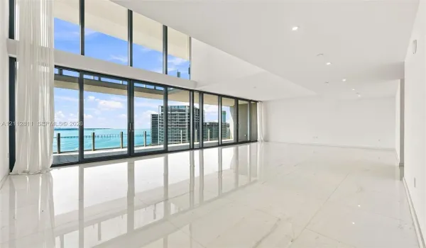 Living room with Double-height floor-to-ceiling windows, polished large-format tile flooring, recessed lighting, and expansive glass sliding doors opening to a private balcony