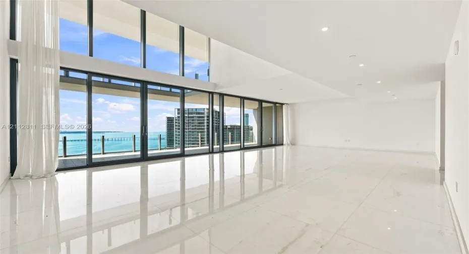 Living room with Double-height floor-to-ceiling windows, polished large-format tile flooring, recessed lighting, and expansive glass sliding doors opening to a private balcony