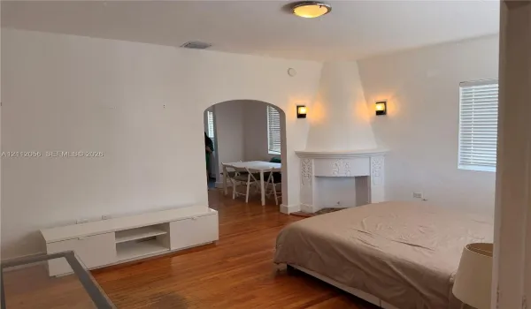 Interior room featuring wood-finish flooring, a decorative corner fireplace with intricate detailing, arched doorway, and white wall-mounted light fixtures