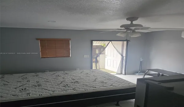 Neutral-toned interior space featuring light-colored tile flooring, a multi-blade ceiling fan with integrated lighting, a single-hung window with wood-finish blinds, and a paneled exterior door