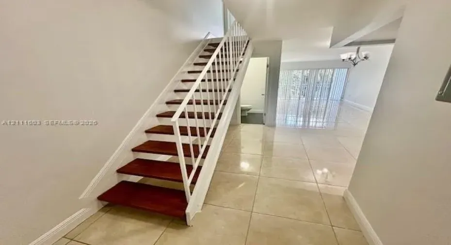 Staircase featuring wood-finish treads and white metal railings, complemented by large-format tile flooring