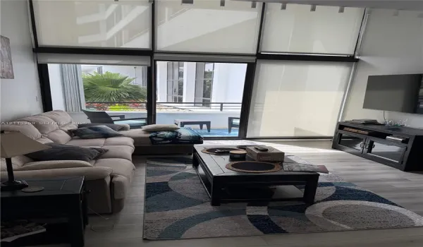 Floor-to-ceiling windows with roller shades, wood-finish flooring, and sliding glass door opening to a private balcony