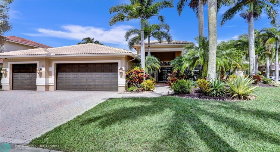 Expansive lawn creates gorgeous curb appeal; manicured landscaping in entrance, flanked by balmy palms.