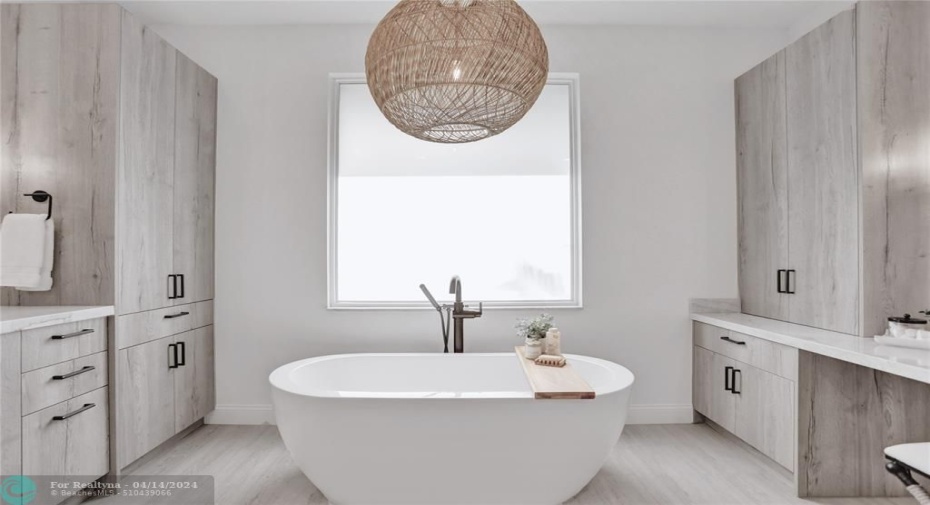 Centered by a Serena & Lily chandelier, the free-standing Wyndham Soho tub is framed by the frosted impact glass window.
