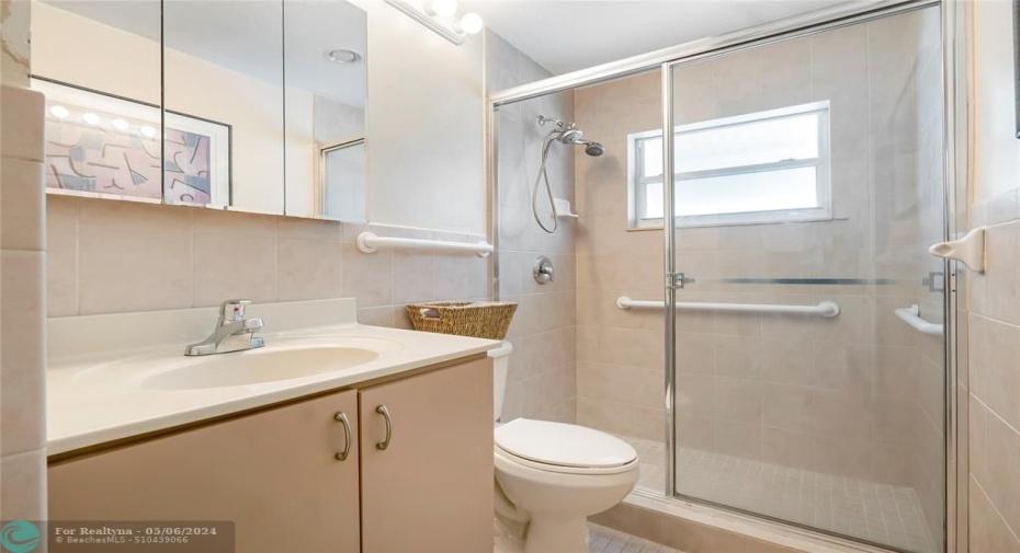 The guest bathroom features elegant glass doors enclosing the spacious shower, complemented by a large vanity for added convenience and comfort.