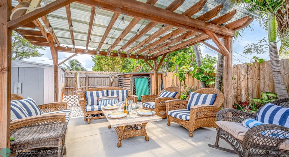 Covered sitting area under pergola with lights, extra storage for yard tools plus shed.