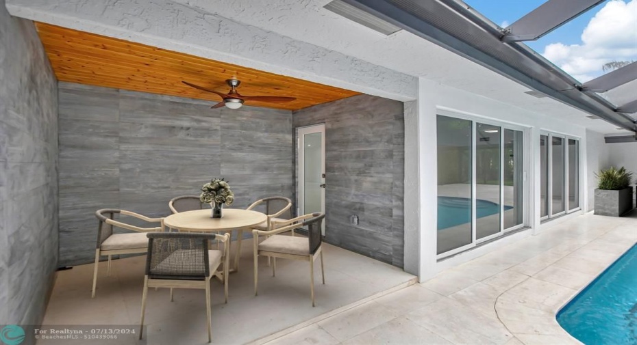 Covered patio with wood ceiling and stone wall.