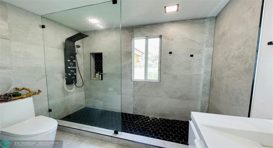The centerpiece of the bathroom is a spacious walk-in shower with a glass enclosure. The shower features large, light gray tiles on the walls and a black hexagonal tile floor, creating a striking contrast and adding a touch of elegance.